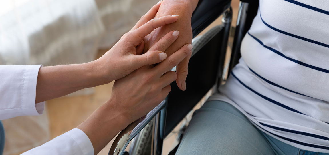 woman holding hands of patient in wheelchair